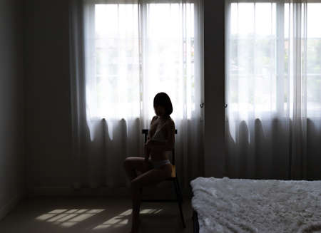 Silhouette asian young woman wearing sexy bikini and sitting on chair in bedroom.の写真素材