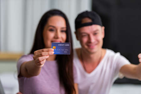 Happy couple is using a laptop and credit card for online shopping while resting on couch at home.の写真素材