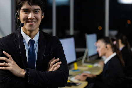 Businessman wearing headphone headset working overtime late at night in call center office with colleague team. Concept for business at night.の写真素材