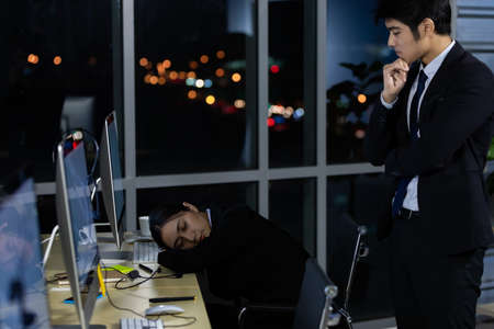 The manager standing behind the employees who secretly slept during working hours in office at night.の写真素材