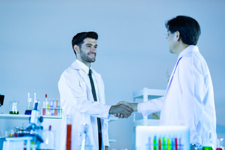 Two scientists shaking hands positivity success happiness. Concept collaboration between Caucasians and Asians scientists.の写真素材