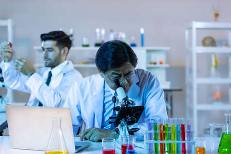 Microbiologist biotechnology researcher or medical worker team look microscope in the lab for researching chemical data by asian scientist.の写真素材