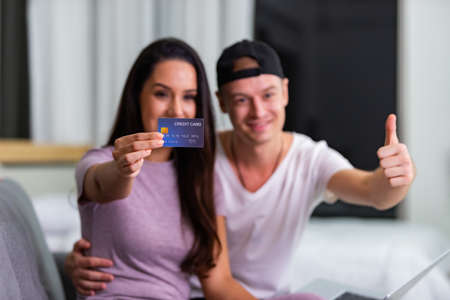 Happy couple is using a laptop and credit card for online shopping while resting on couch at home.の写真素材