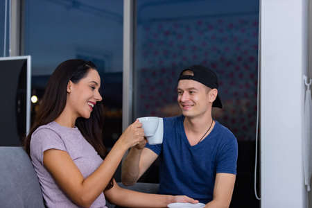 Happy couple husband and wife are sitting at home in the living room, talking relax and drink tea late at night.の写真素材