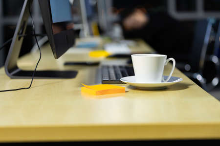 Business office desk with coffee cup and city light bokeh background. Overtime working desk without people.の写真素材