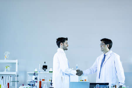 Two scientists shaking hands positivity success happiness. Concept collaboration between Caucasians and Asians scientists.の写真素材