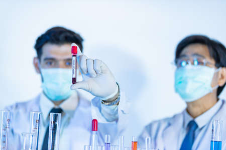Scientist in sterilizes lab holding Covid-19 test tube sample in hand. Selective focus on the name of virus. Concept for medical people trying and researching for win over coronavirus.の写真素材