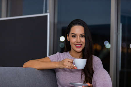 Woman enjoying a cup of tea in the night sitting on a couch in the living room at homeの写真素材