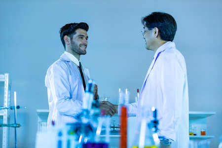 Two scientists shaking hands positivity success happiness. Concept collaboration between Caucasians and Asians scientists.の写真素材
