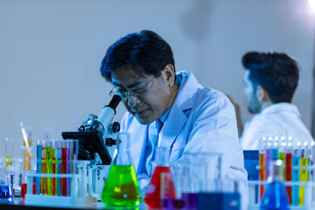 Microbiologist biotechnology researcher or medical worker team look microscope in the lab for researching chemical data by asian scientist.の写真素材