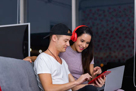 Happy couple enjoying media content in a smart phone sitting on a couch at homeの写真素材