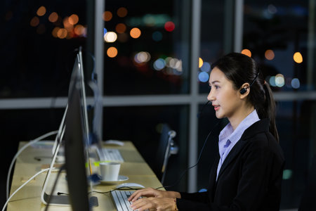 Asian young woman wearing headphone headset working overtime late at night in call center office. Concept for business at night.の写真素材