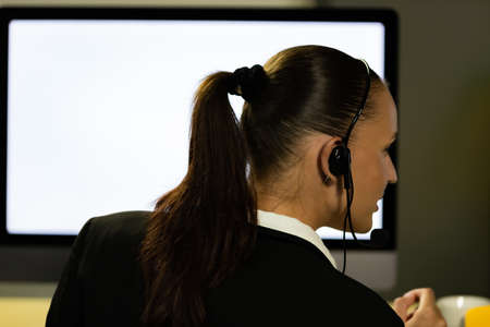 Caucasian young woman wearing headphone headset working overtime late at night in call center office with her colleague team. Concept for business at night.の写真素材