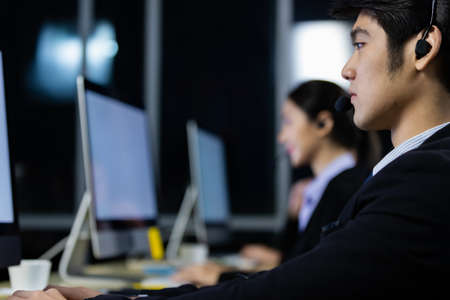 Businessman wearing headphone headset working overtime late at night in call center office with...