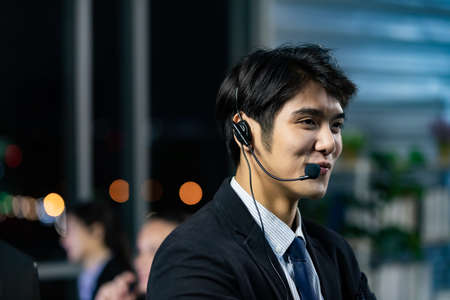 Businessman wearing headphone headset working overtime late at night in call center office with colleague team. Concept for business at night.の写真素材