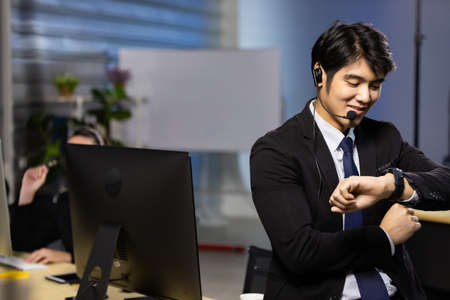 Businessman looking at the time on his wrist watch in call center office at night. Overtime working...