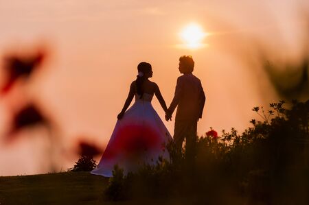 Asian Bride and Groom Standing on Mountain at Sunsetの写真素材