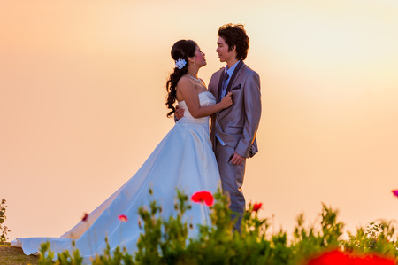 Asian Bride and Groom Standing on Mountain at Sunsetの写真素材