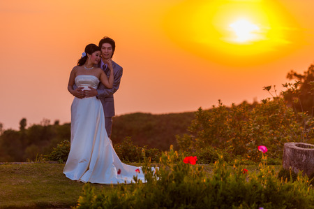 Asian Bride and Groom Standing on Mountain at Sunsetの写真素材