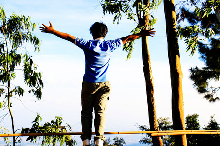 Rear view portrait of young man standing on a mountain with arms spread openの写真素材