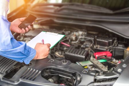 Hand mechanic hold check sheet paper and smart phone for basic checking a engine of car,maintenance...