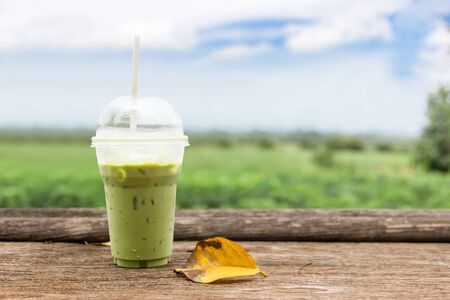 Ice green tea in the plastic cup on the wood bar in coffee shop with nature green leaf and blue sky