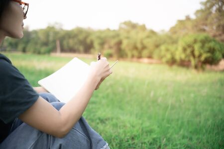 Close up hand women and pencil in hand white on notebook and blur background in gardenの写真素材