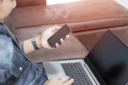 Home business concept of a man use smartphone and laptop computer and sat on the sofa