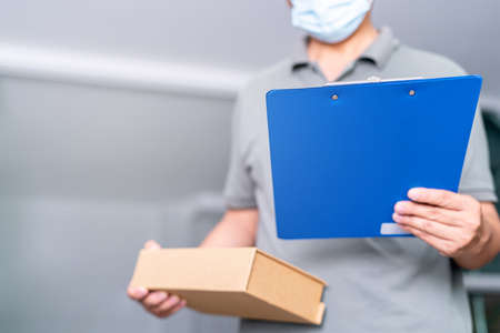 Delivery man hold the file and shopping box in home and protective mask for protection in delivery workの写真素材