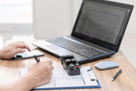 Technician use pen mark on checklist about spare parts Auto glass adjustment switch kit and search technical data with smart phone and laptop in car service officeの写真素材