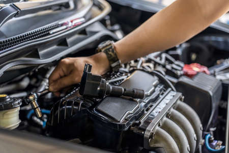 Close up spark plug coil on engine cover and a man use block wrench remove a bolt for take off coil engine service in garage and engine room  backgroundの写真素材