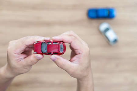 Damaged toy car in the man's hand and new car on the floor : accident comparison of car toyの写真素材