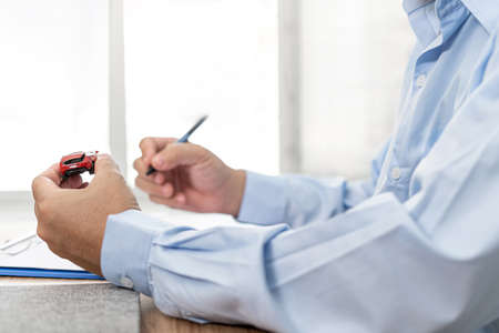Car insurance concept : Man pen write insurance documents and a accident toy car on wood tableの写真素材