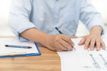 Engineering work concept : Close up hand a use pencil mark CAD drawing and calculator in Calculating document on the wood tableの写真素材