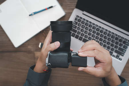A man inserts battery into camera and use laptop computer in photography work