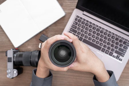 Close up camera lens in hand a man and photography equipment on vintage wood table : photo work conceptの写真素材