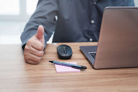 Business man thumbs up for work on the project successfully using computer and writing on a paper on desk in officeの写真素材