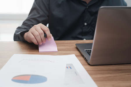 Business man write notes on paper   and use laptop computer calculate and analyzing with document data graph for new project of business strategy at workplace.の写真素材