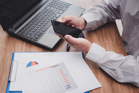 Business man use smartphone analyzing business work on document data graph with laptop computer...