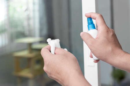 A man press alcohol bottle spray for cleaning door handle and use white lint cleaning and primary disease prevention  in homeの写真素材