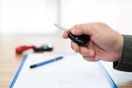 Close up hand of man holding and push remote control for lock and Un-lock car and insurance document on table : concept model toy a car in blur backgroundの写真素材