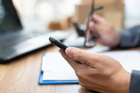 The postal courier checks the order balance on smartphone and check list on a white paper file before product deliveryの写真素材