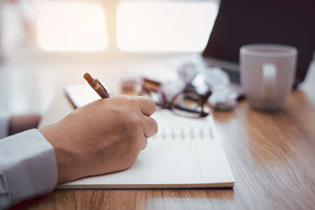 A man use pencil write on notebook paper and crumple paper laptop computer glasses coffee cup on...