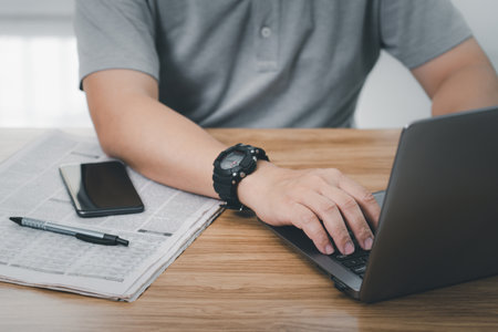 A man typing and search with important news on laptop in the internet on computer Compared to daily newspapers in office workの写真素材