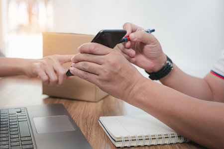 Parcel delivery staff hold smartphones and is giving customers the ability to check the correct items to deliver parcels in the parcel delivery officeの写真素材