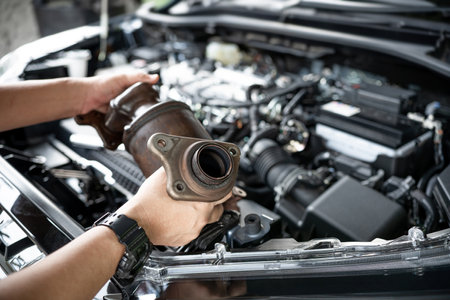Close up old catalytic converter in hand Car service man remove from engine gasoline car dust clogged condition on filter in service concept and engine room in the backgroundの写真素材