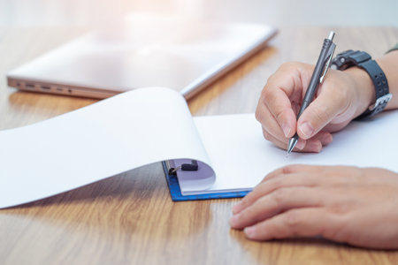 Close up hand a man write on notebook paper and close laptop on table and office blur background ,Traditional memory recording with technologyの写真素材
