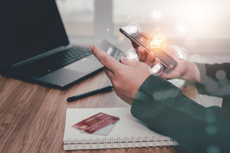 Close up a man holding a credit card and using a smartphone for payment online various expenses in the home office and a credit card laptop on table with business iconの写真素材