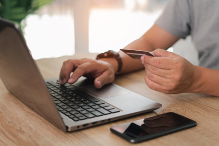 Business man hold credit card and input data for payment to laptop,making online payment through the Internet,smartphone and laptop on wood tableの写真素材