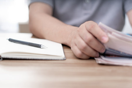 Close up pen on notebook and a man looking newspaper on the wood tableの写真素材